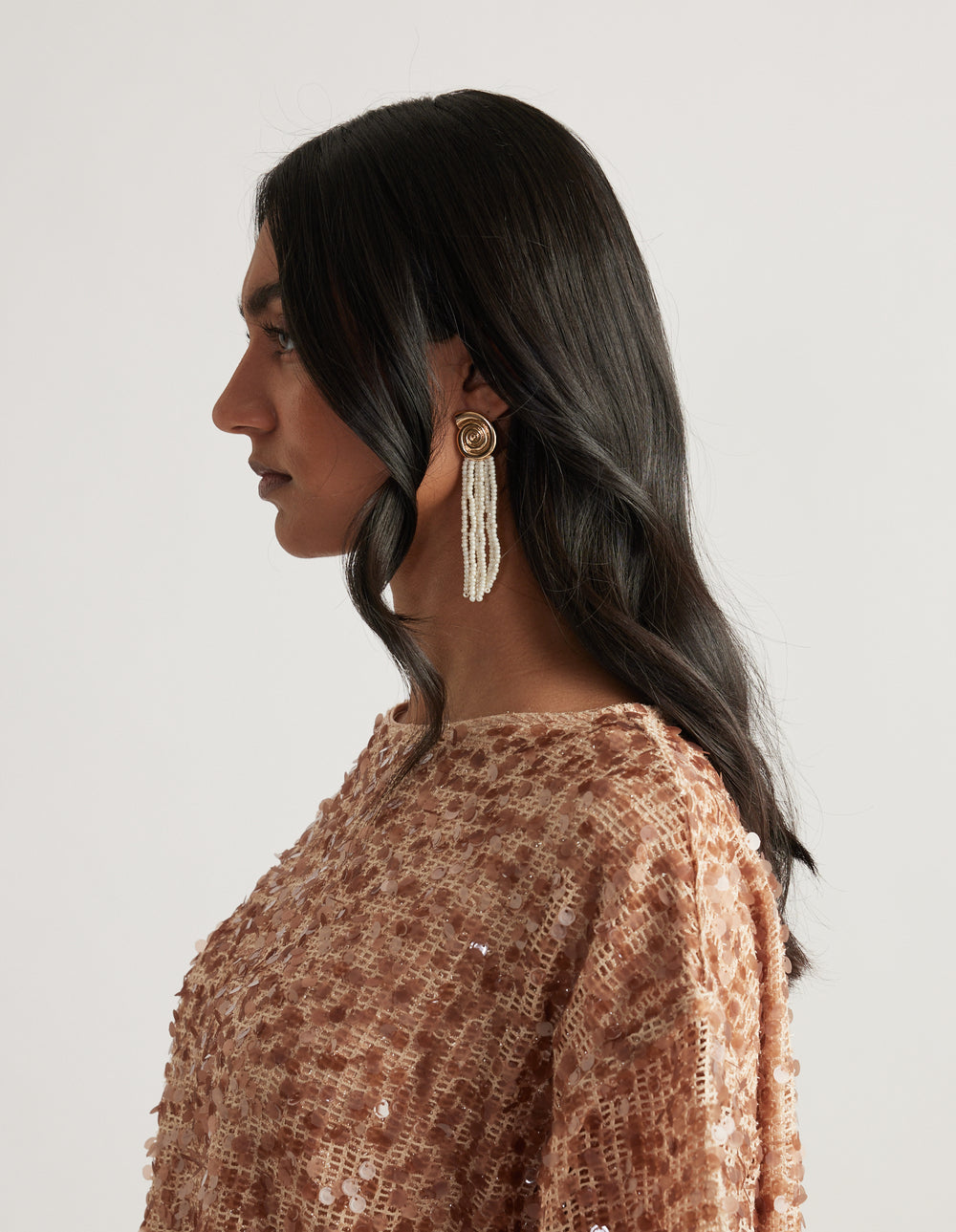 Woman shown in profile wearing a gold stud earring with long beaded tassels