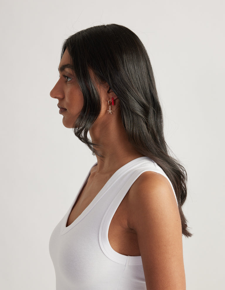 Woman in profile wearing red bead hoop and starfish earrings with a white tank top