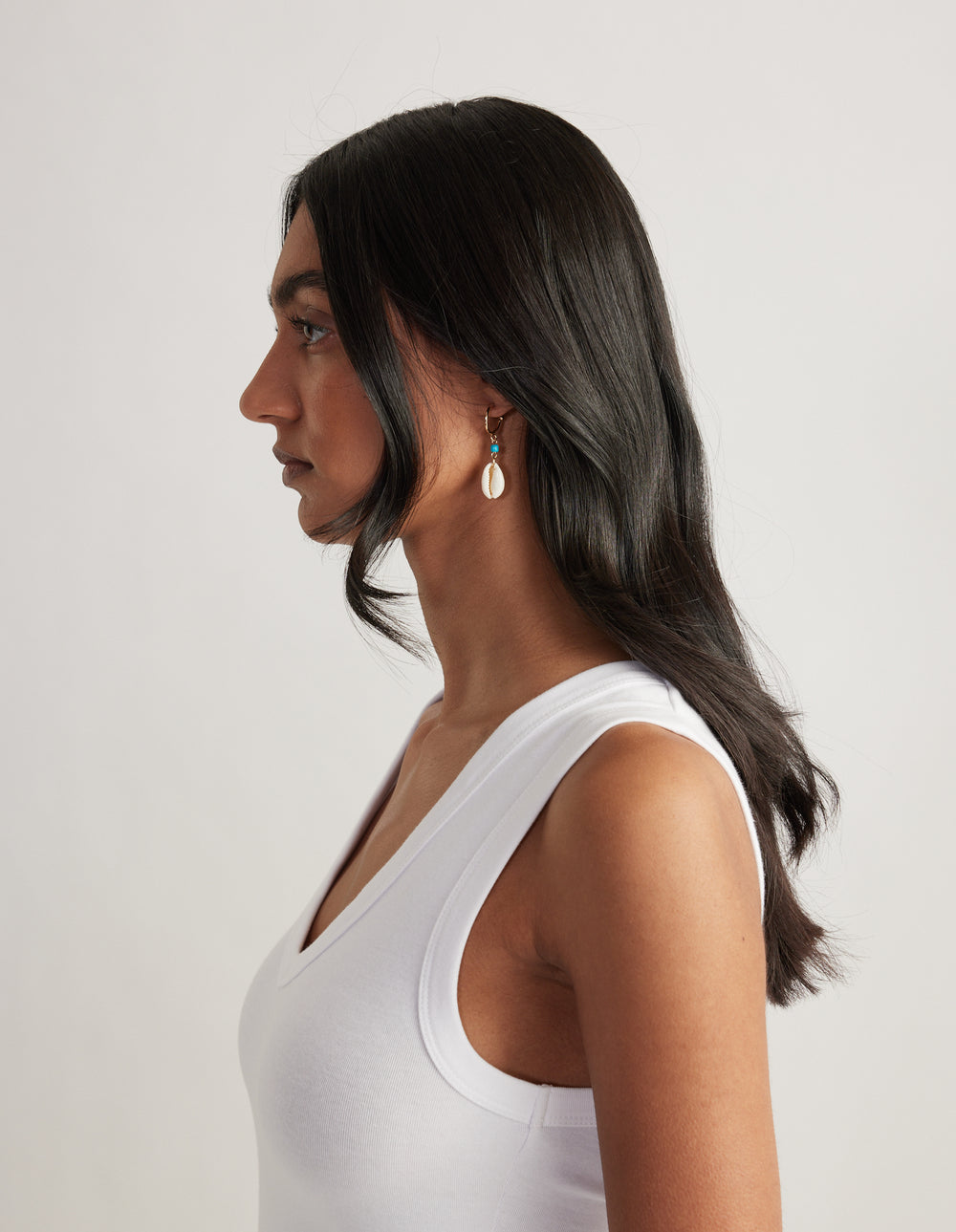 Model in profile wearing a small red bead hoop earring with a dangling shell charm