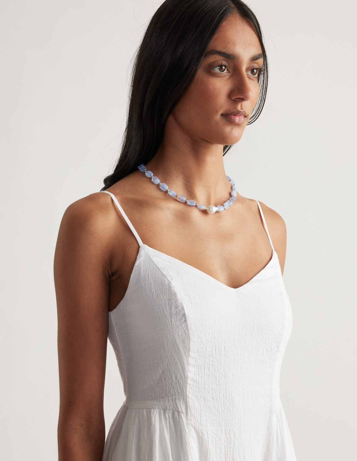 Woman wearing a light blue oval bead necklace with pearl accents over a white camisole