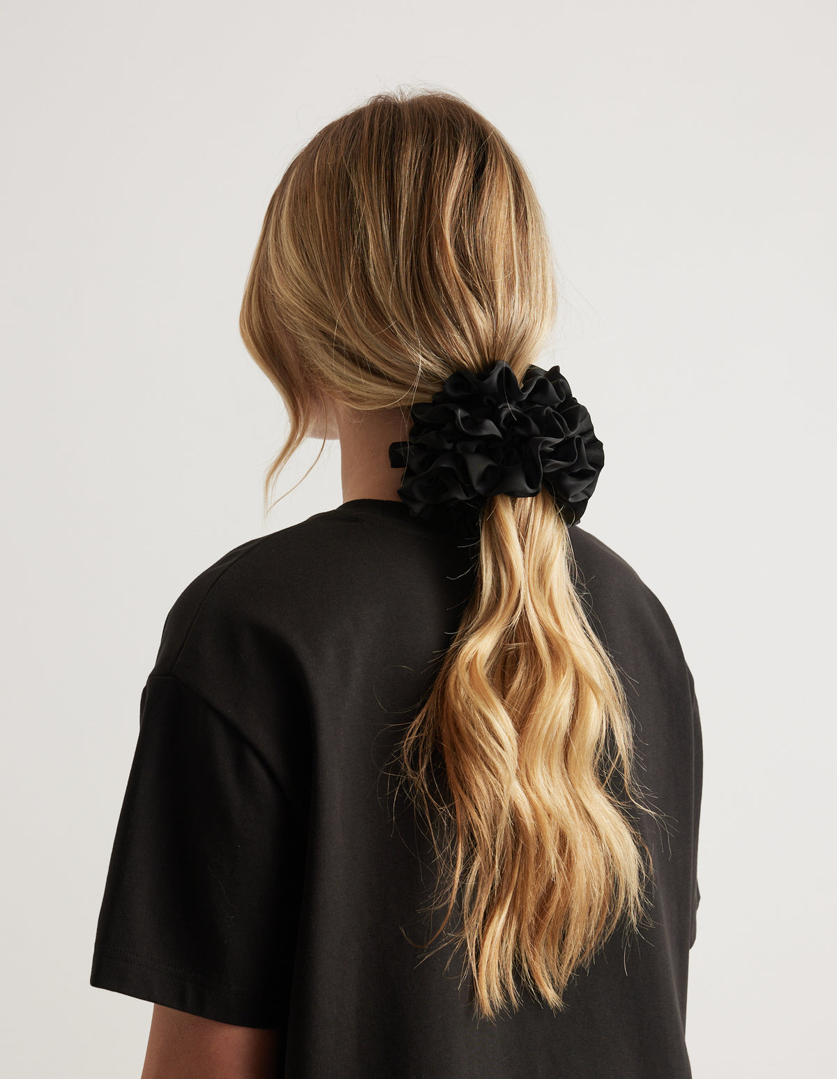 Back view of a woman wearing a black ruffled scrunchie in a long blonde ponytail with a black tee