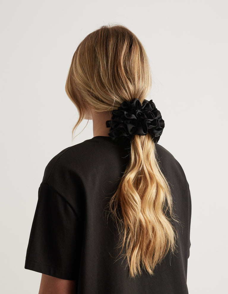 Back view of a woman wearing a black ruffled scrunchie in a long blonde ponytail with a black tee