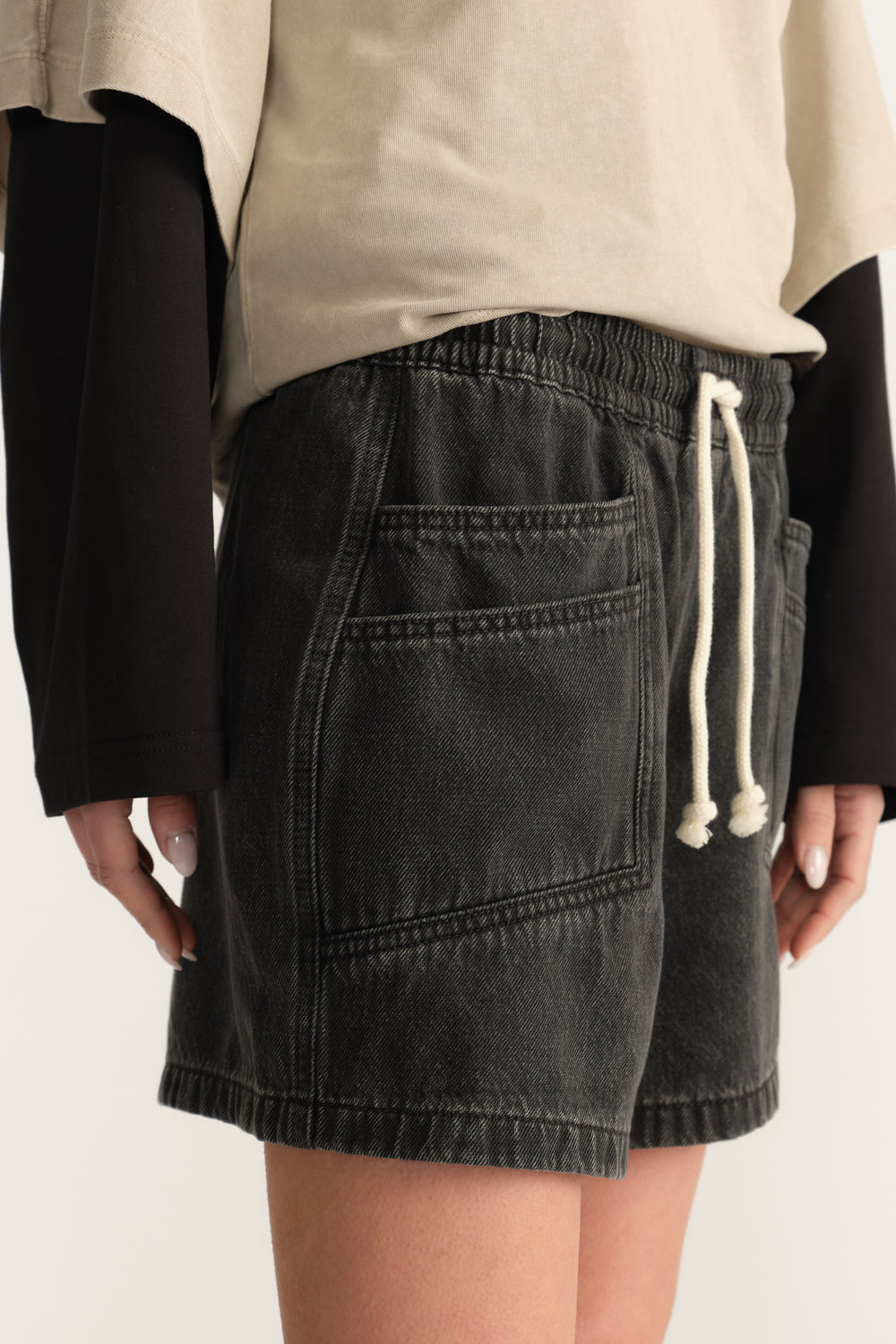 Woman wearing black denim shorts with an elasticated drawstring waist and patch pocket