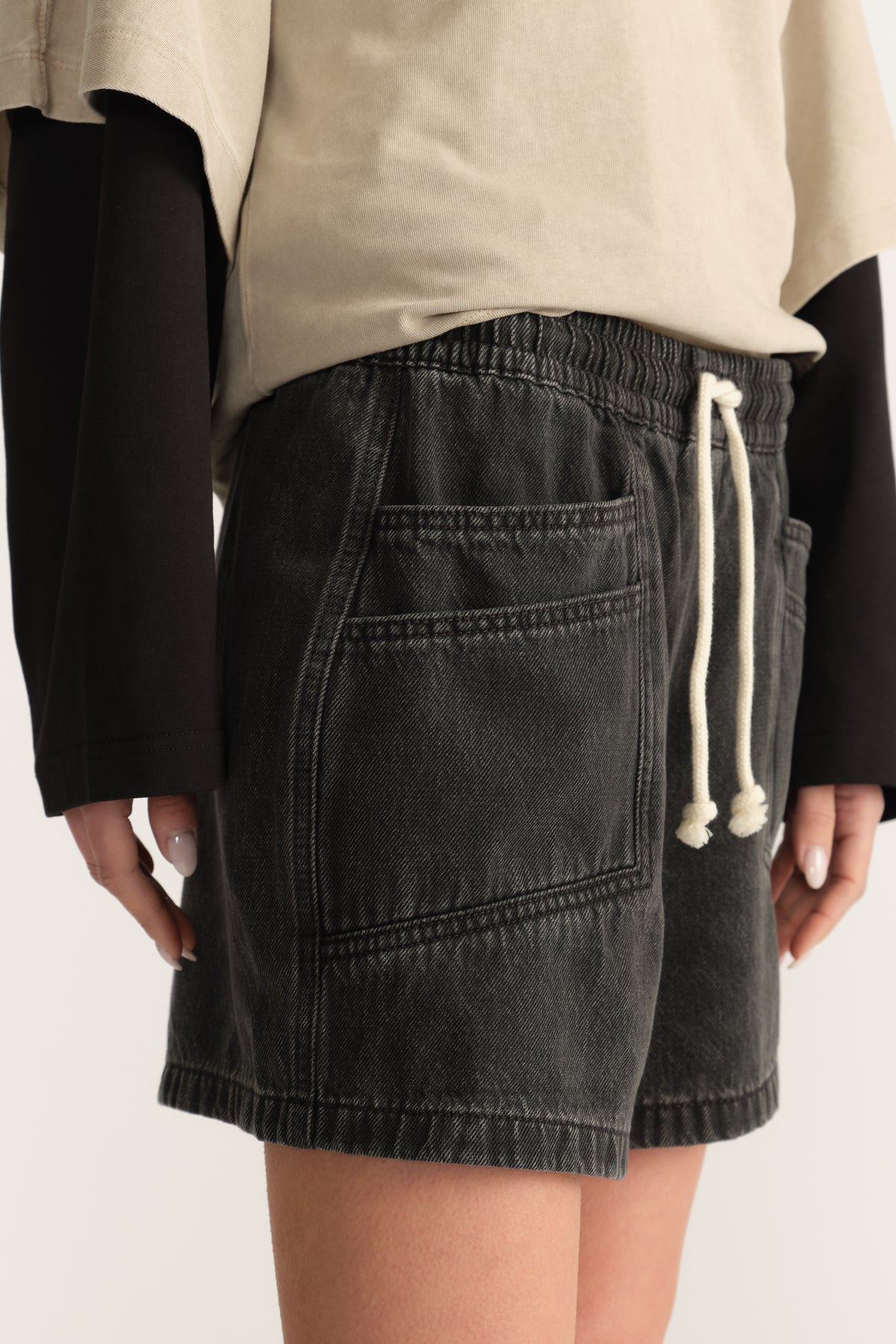 Woman wearing black denim shorts with an elasticated drawstring waist and patch pocket