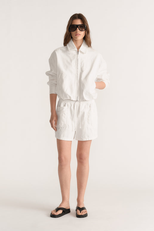 Woman wearing white denim pull on shorts with an elastic waist, zip jacket and black sandals