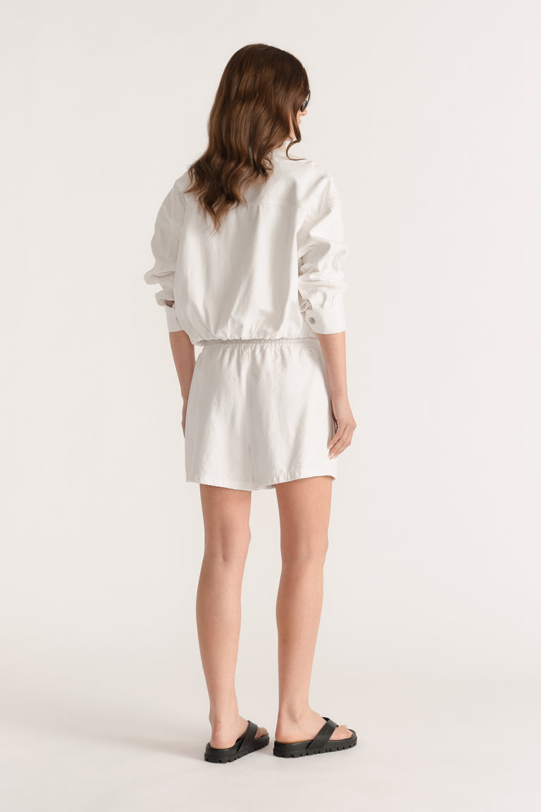 Model seen from behind wearing white elasticated denim shorts with a mid rise waist and black sandals