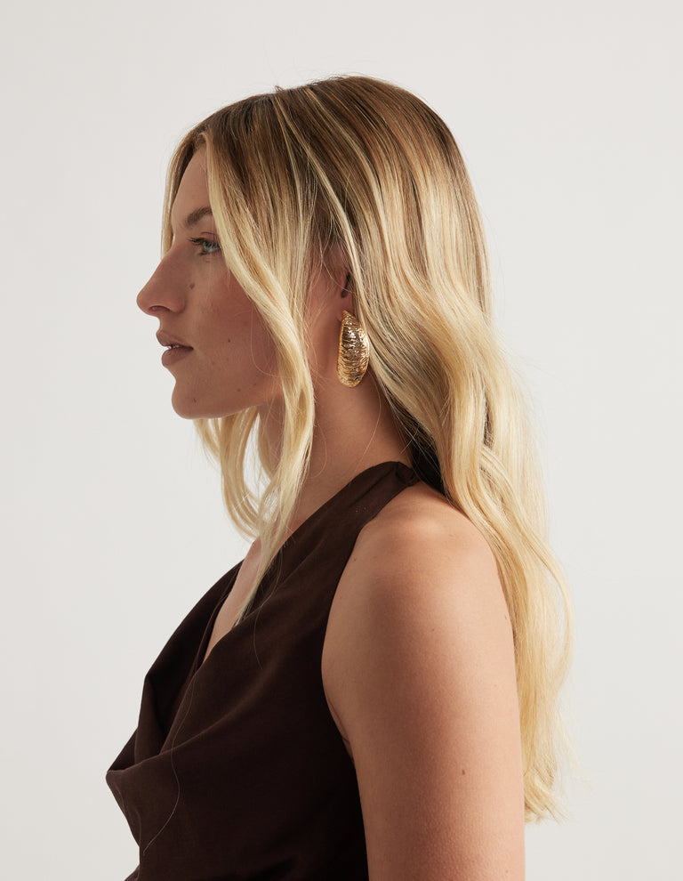 Woman in profile wearing a textured high shine gold shell earring