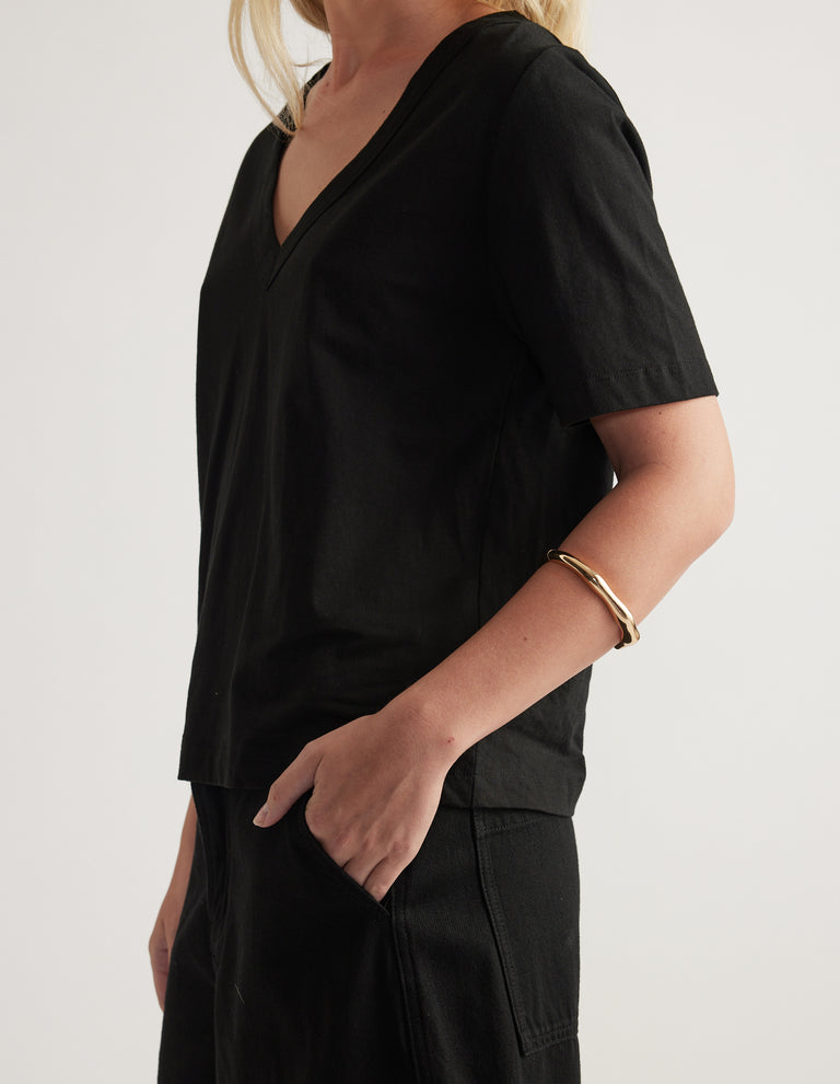 Shiny gold hinge bangle with uneven texture worn on the wrist with a black V neck tee