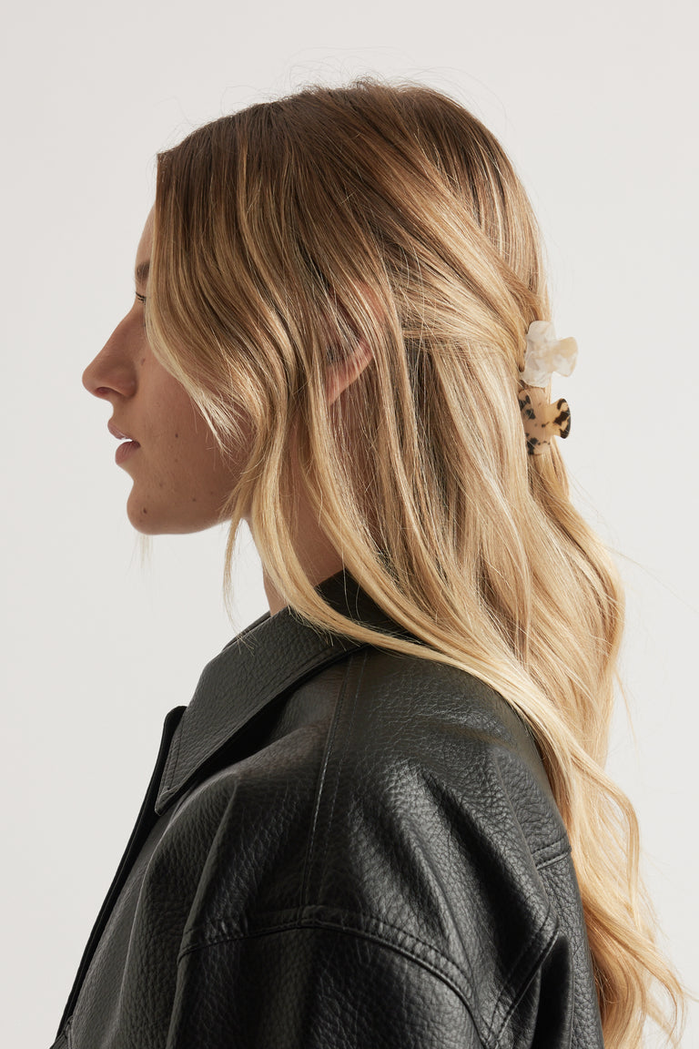 Side profile of woman with blonde hair styled in an abstract claw clip, wearing a black textured jacket
