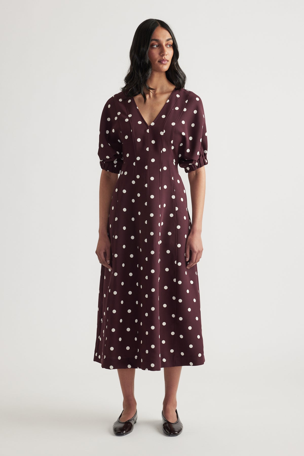 Woman wearing a burgundy polka dot midi dress with puff sleeves and black loafers