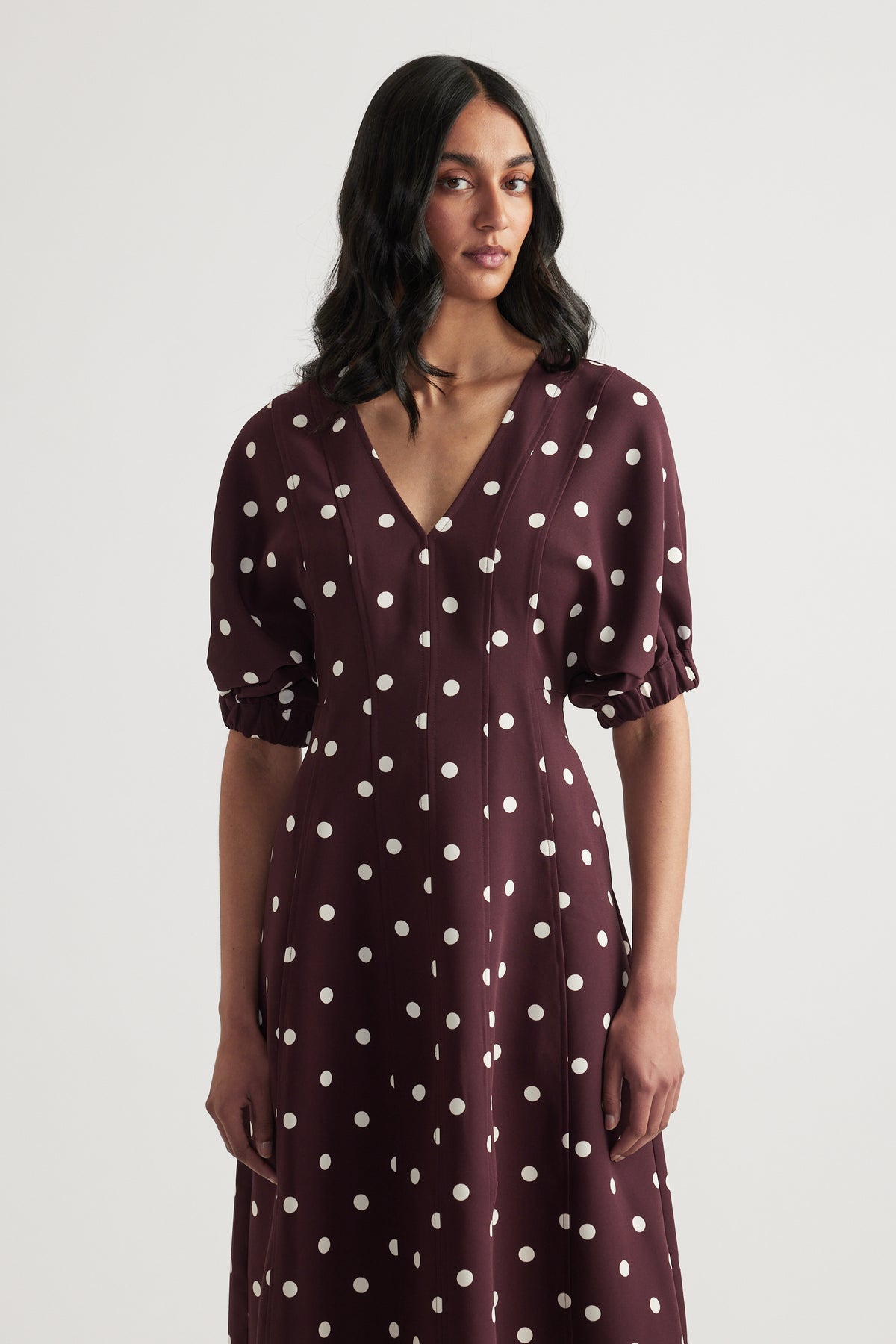 Woman wearing a burgundy polka dot midi dress with a V neck and puff sleeves