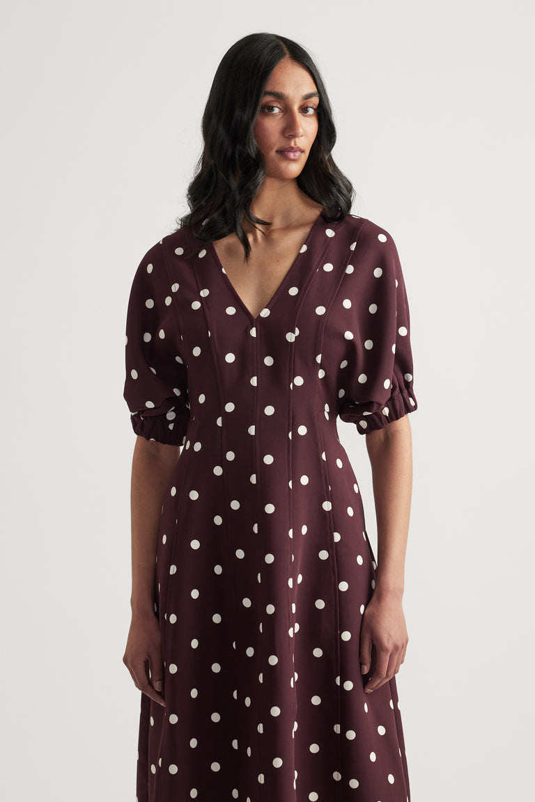 Woman wearing a burgundy polka dot midi dress with a V neck and puff sleeves