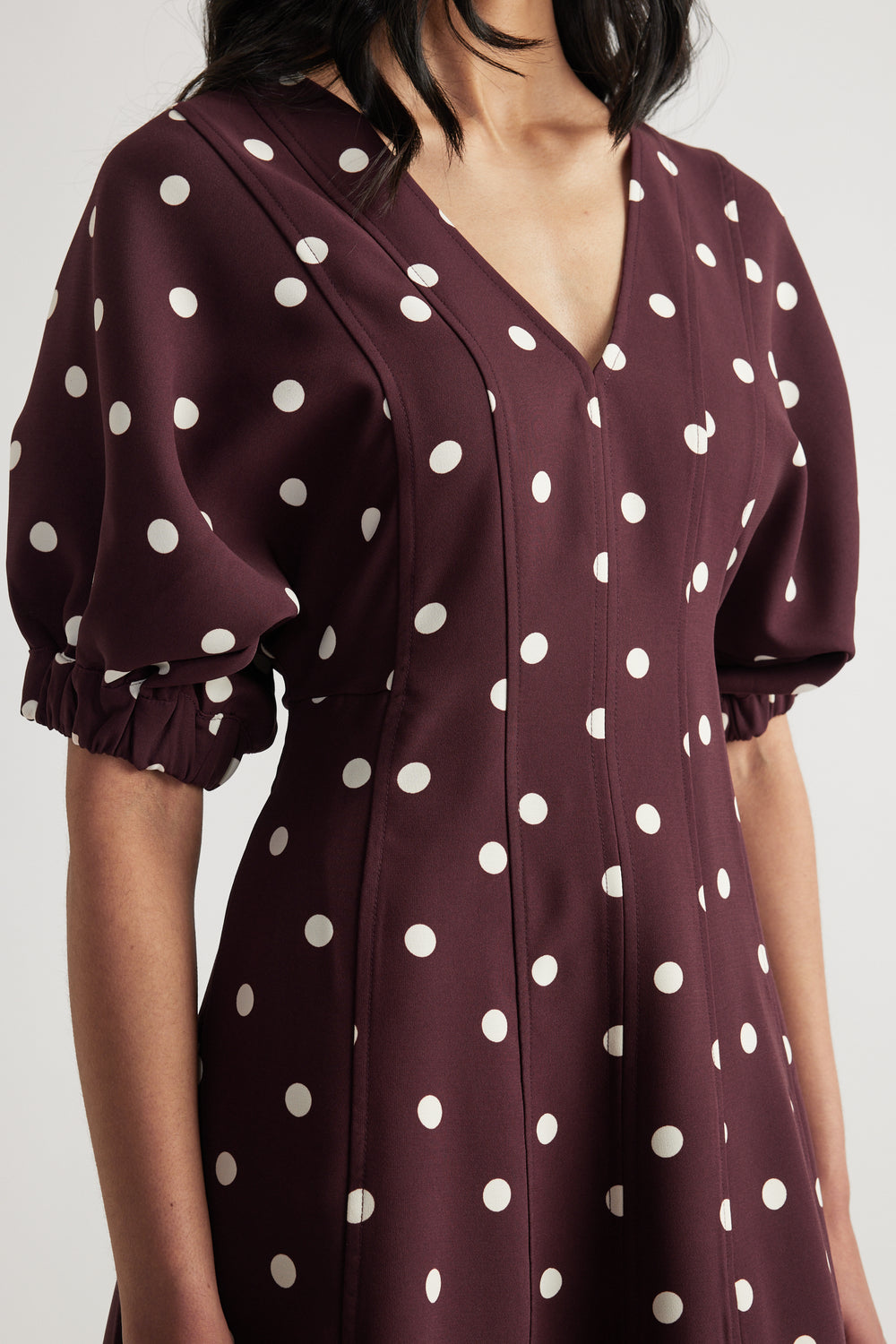 Woman wearing a burgundy polka dot midi dress with a V neckline, puff sleeves and panelled A-line shape