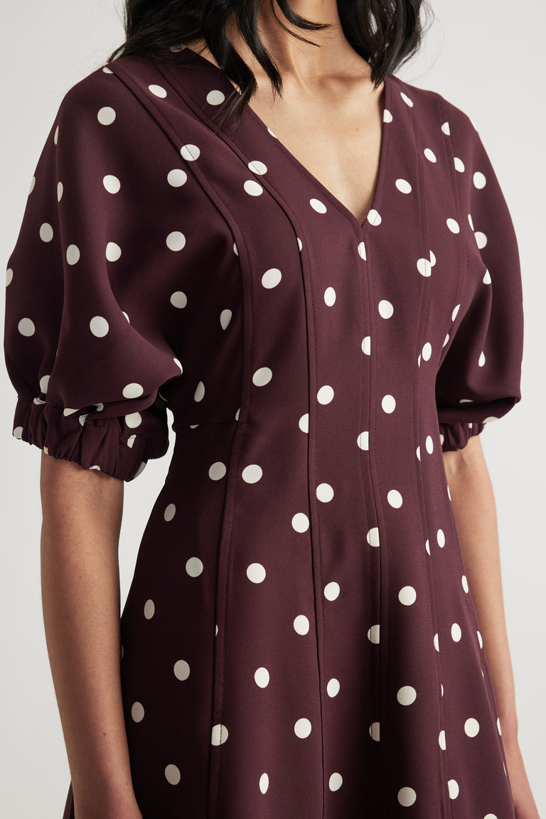 Woman wearing a burgundy polka dot midi dress with a V neckline, puff sleeves and panelled A-line shape