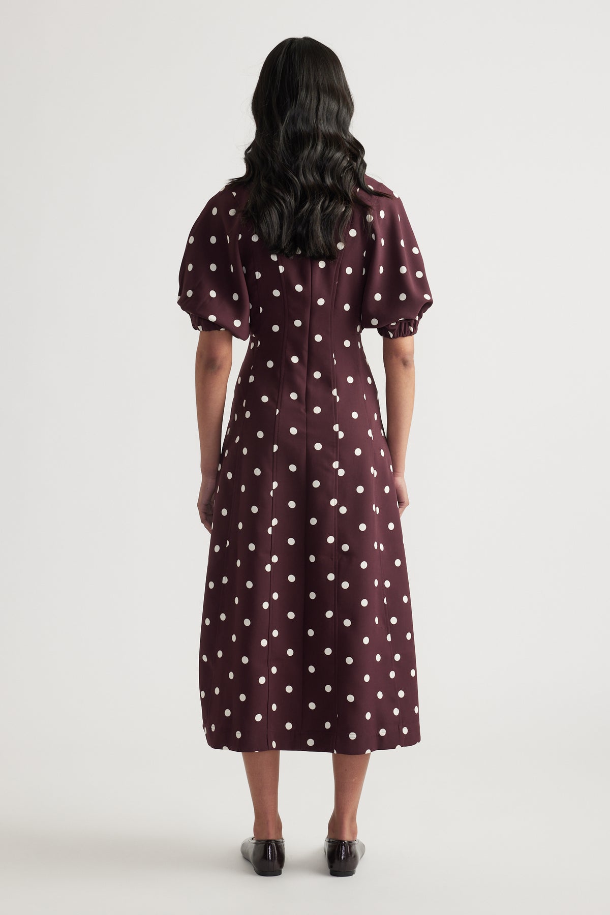 Back view of a woman wearing a burgundy polka dot midi dress with short puff sleeves and an A-line silhouette