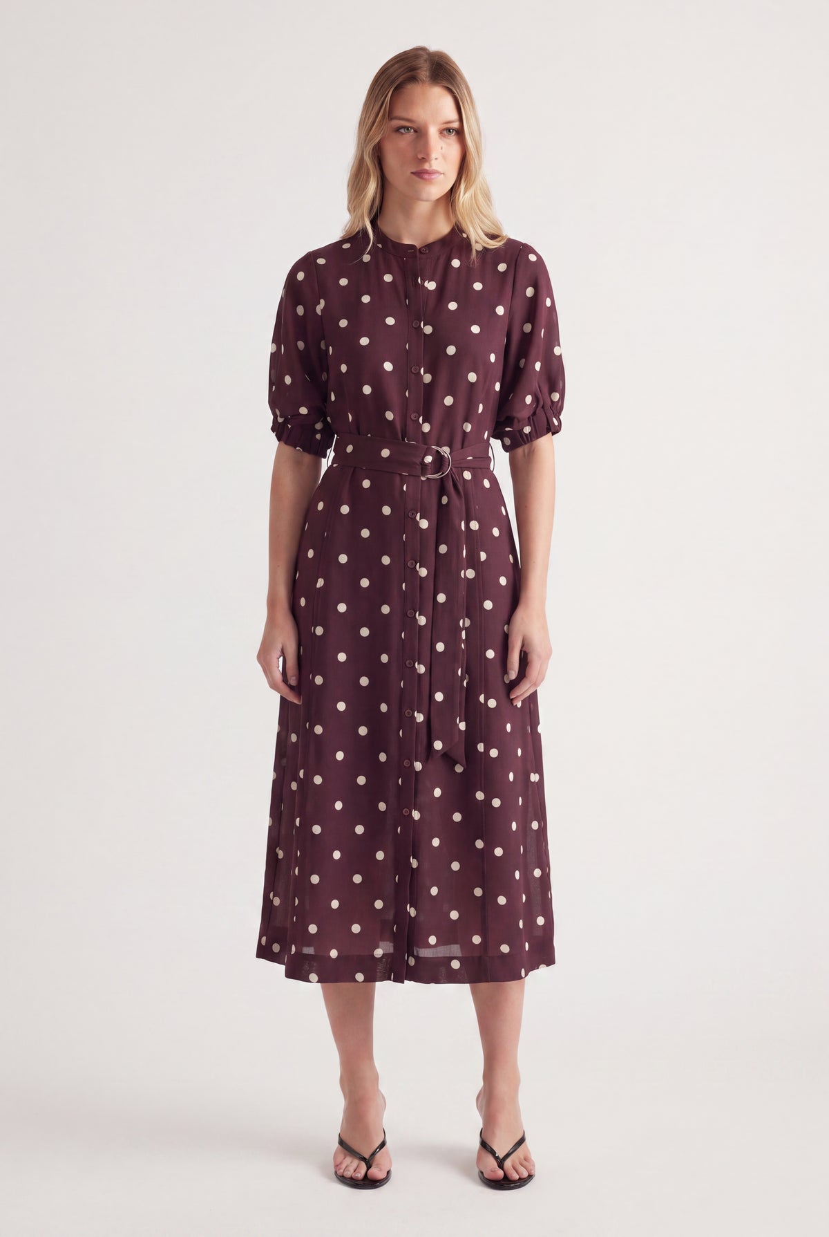 Woman wearing a burgundy polka dot midi dress with puff sleeves and a waist belt