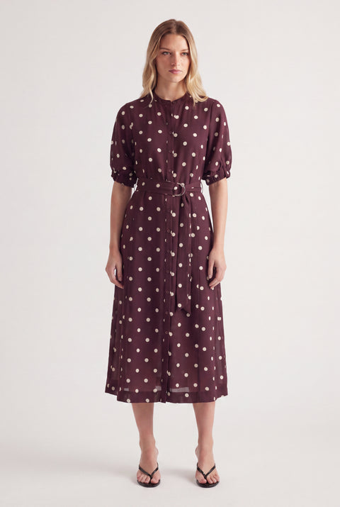 Woman wearing a burgundy polka dot midi dress with puff sleeves and a waist belt