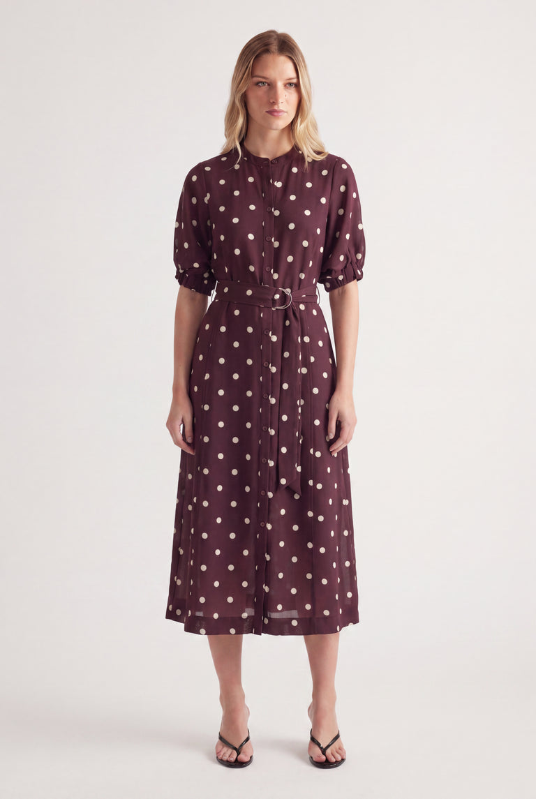 Woman wearing a burgundy polka dot midi dress with puff sleeves and a waist belt