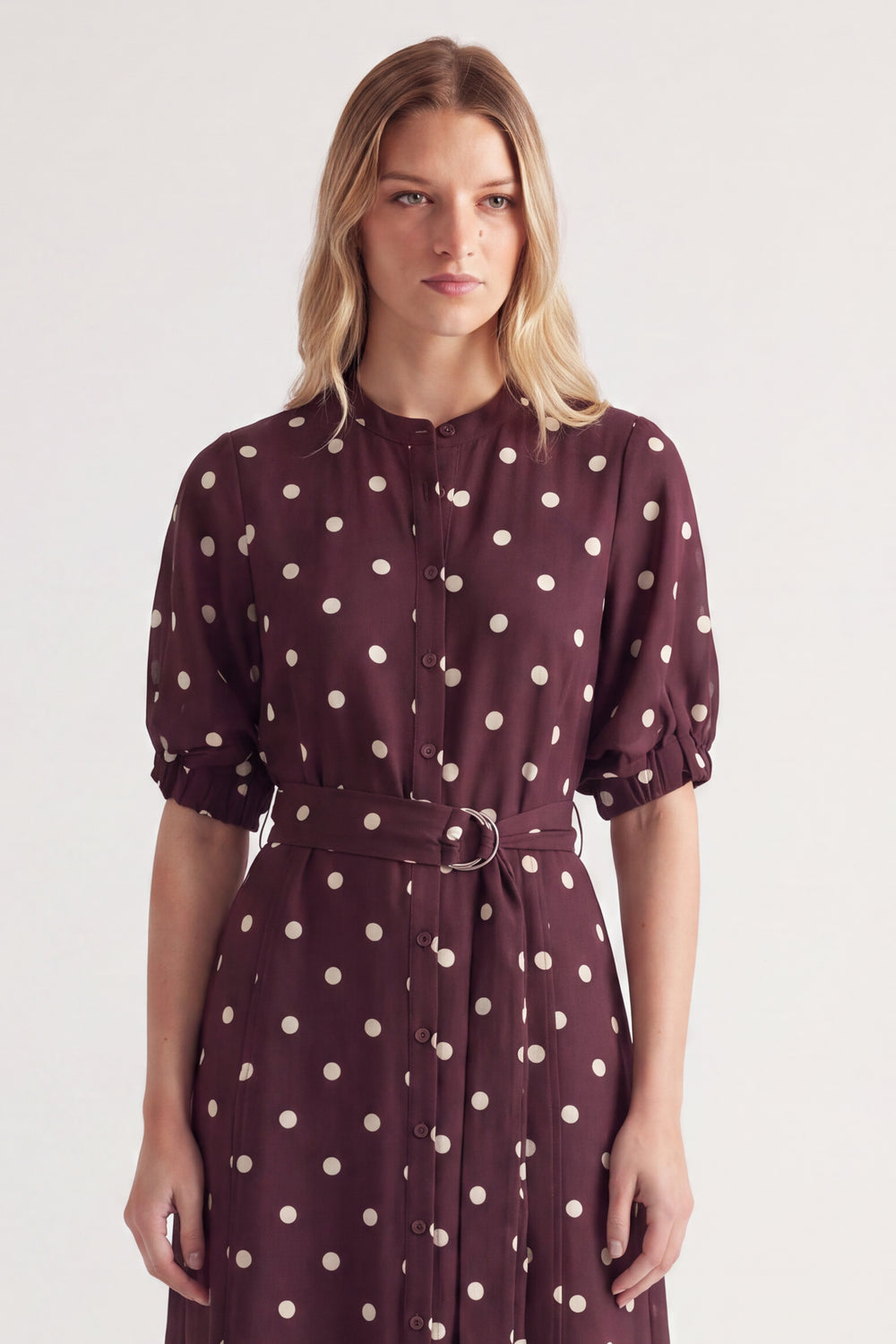 Woman wearing a burgundy polka dot midi dress with puff sleeves and a belted waist
