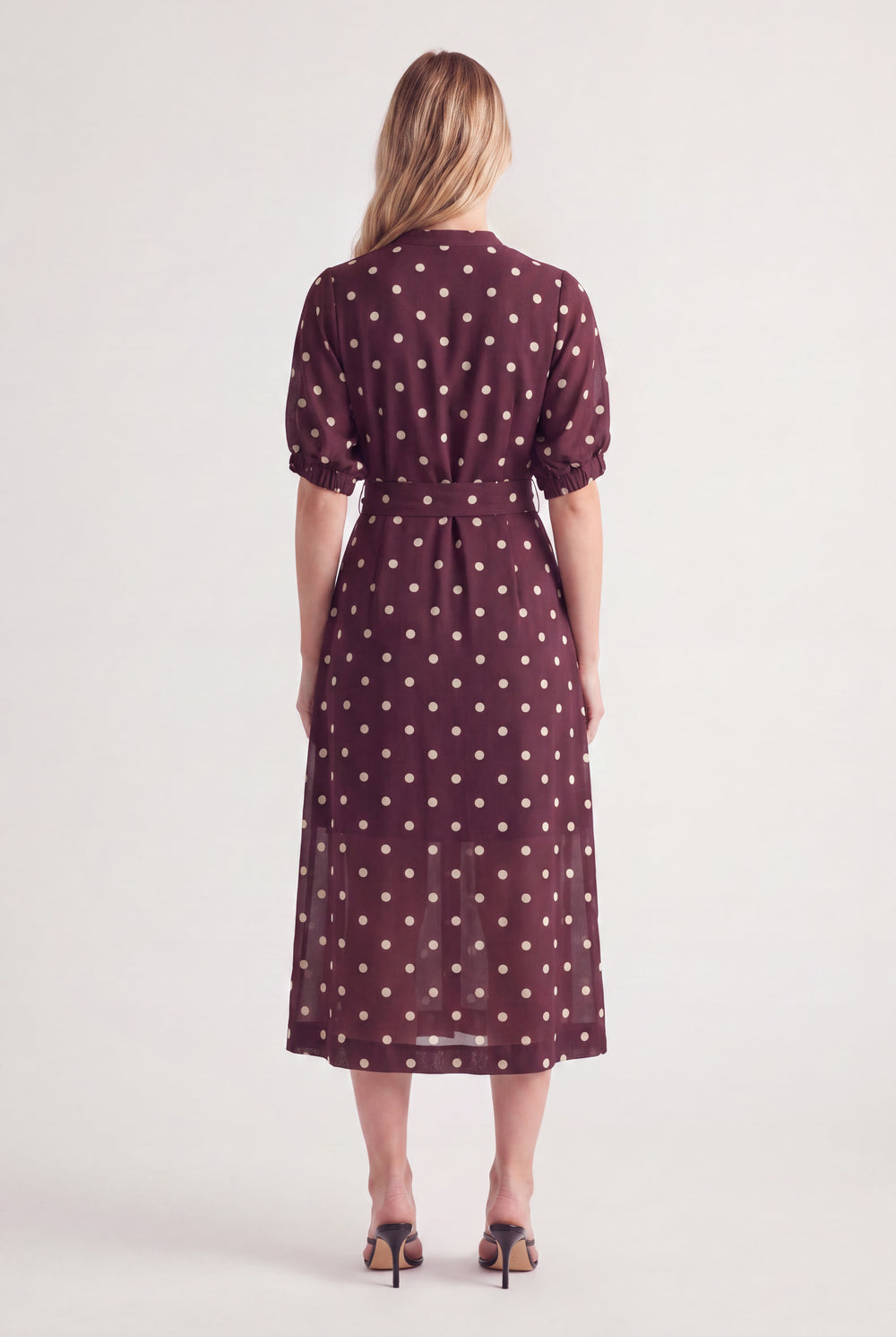 Woman wearing a burgundy polka dot midi dress with puff sleeves and a waist belt