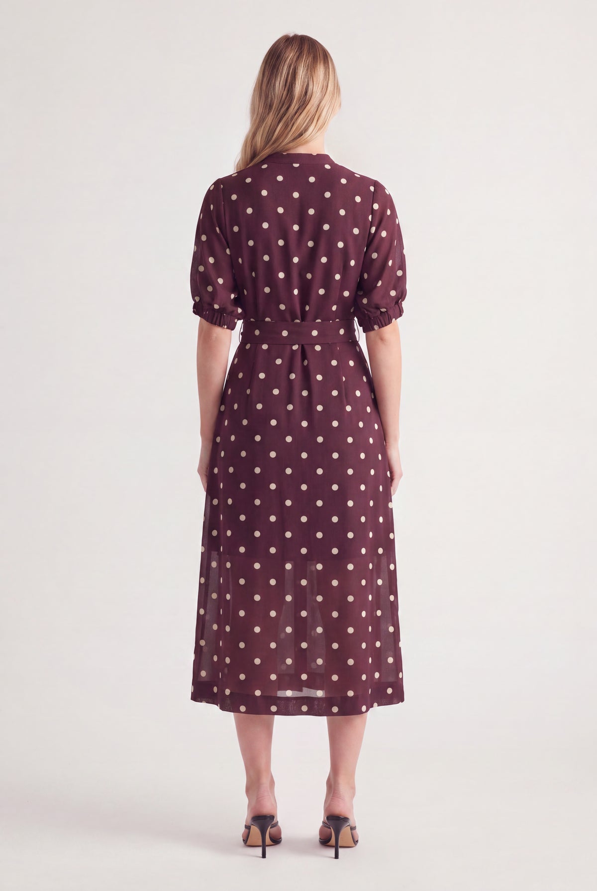 Woman wearing a burgundy polka dot midi dress with puff sleeves and a waist belt
