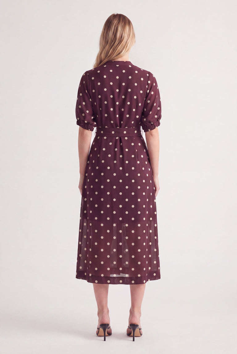 Woman wearing a burgundy polka dot midi dress with puff sleeves and a waist belt