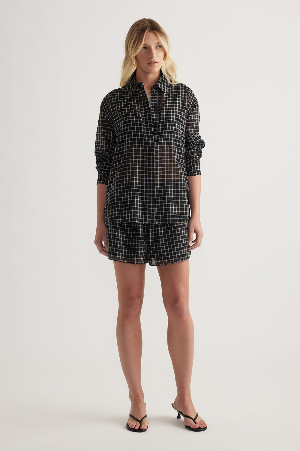 Model wearing a black check oversized shirt with rolled sleeves, matching shorts and strappy sandals