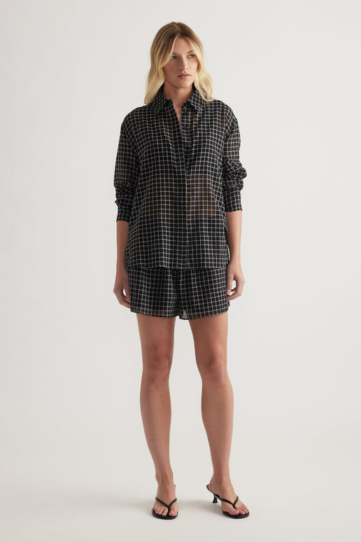 Model wearing a black check oversized shirt with rolled sleeves, matching shorts and strappy sandals