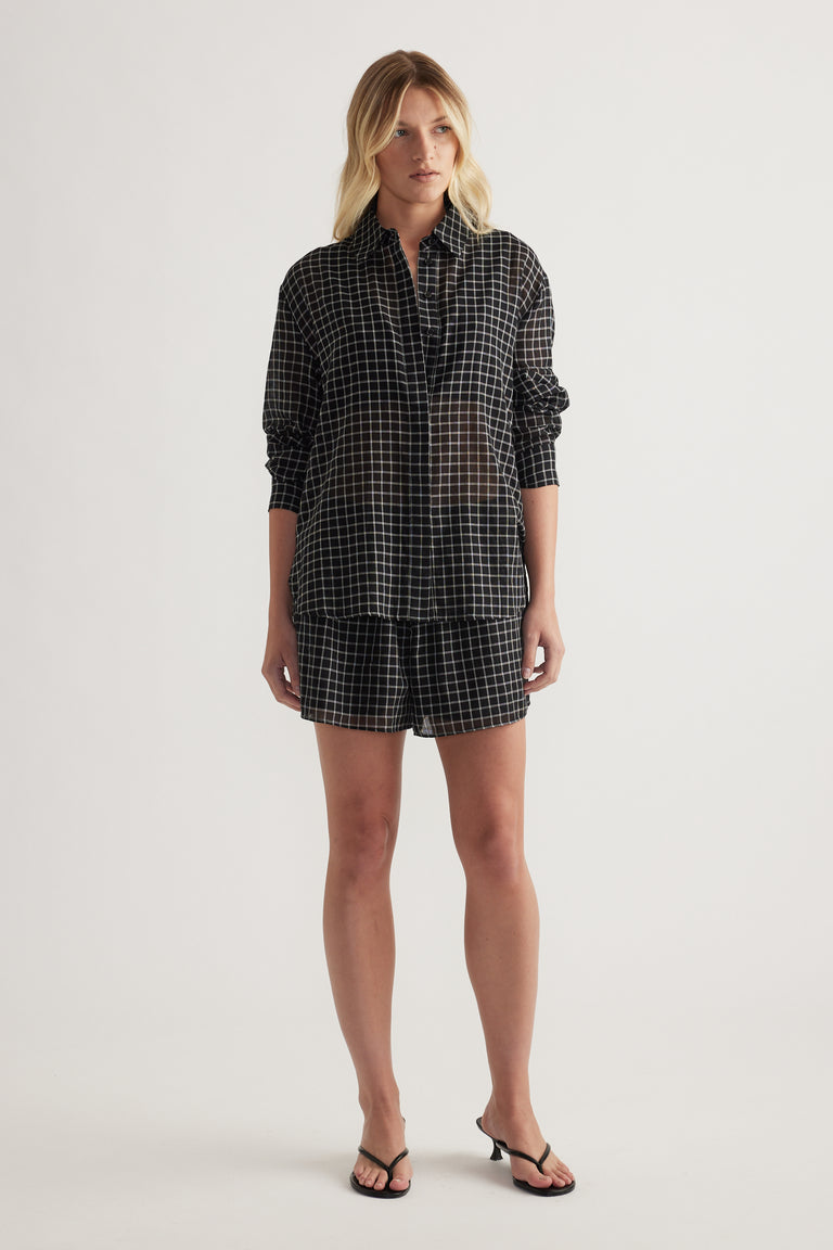 Model wearing a black check oversized shirt with rolled sleeves, matching shorts and strappy sandals