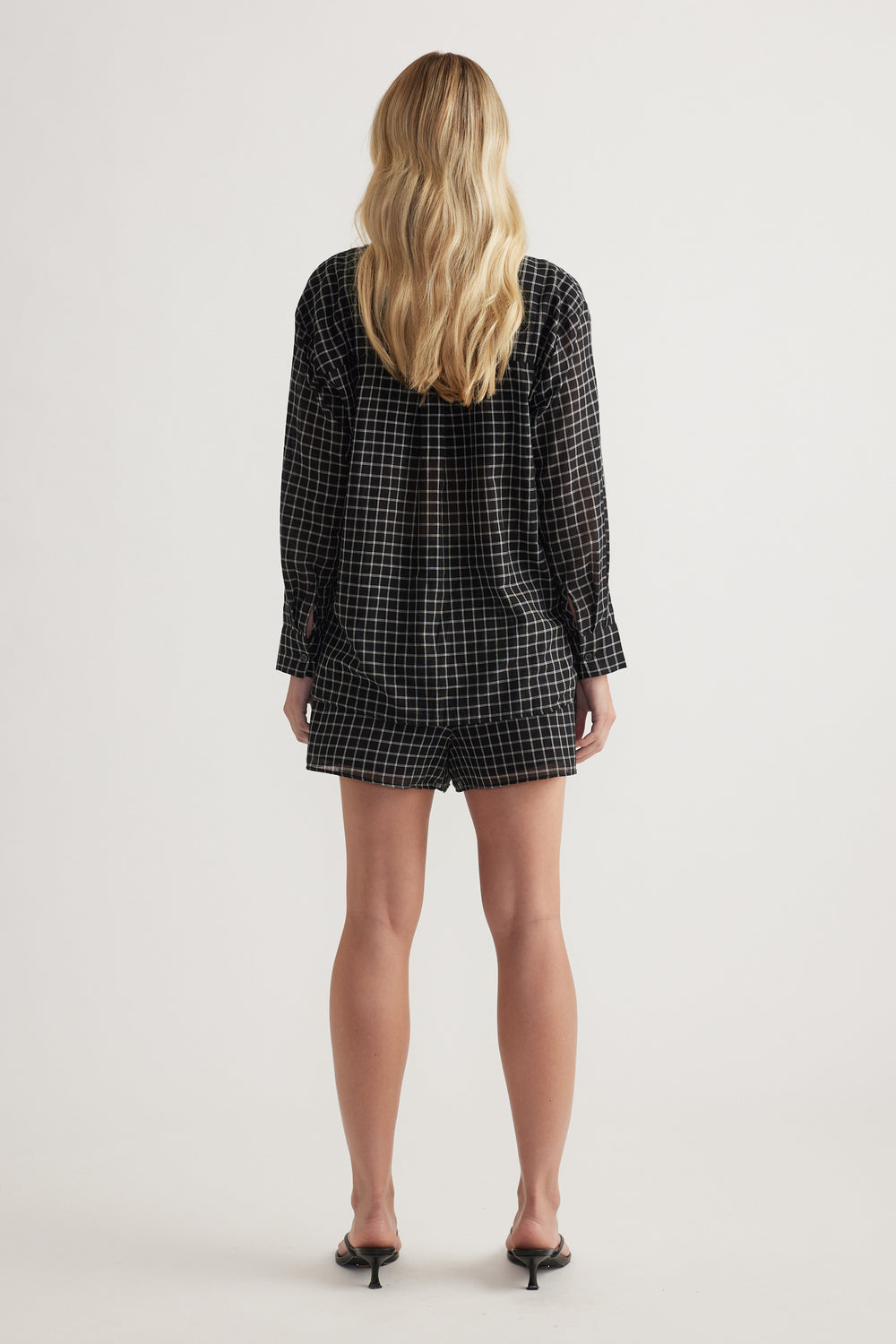 Back view of a model wearing an oversized black check shirt with long sleeves and black shorts