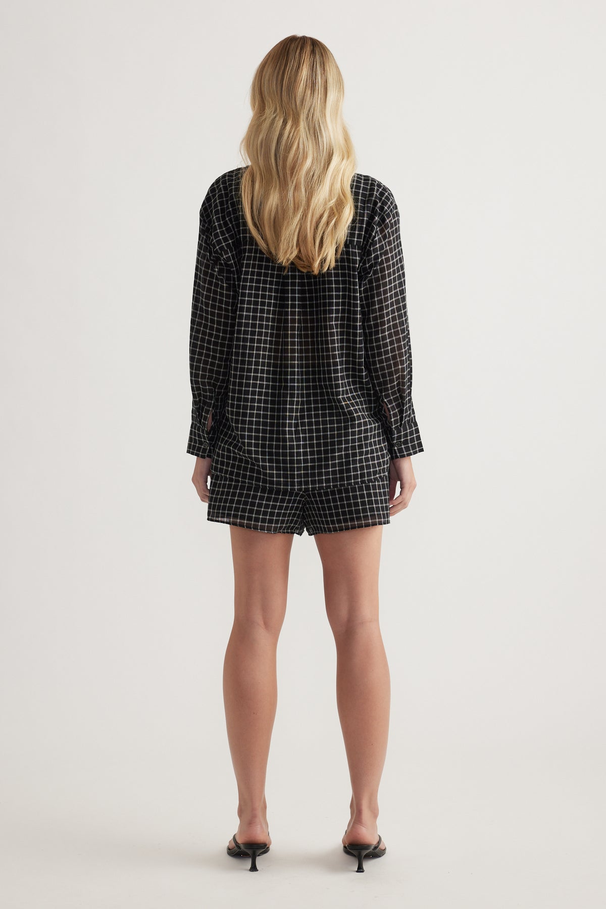 Back view of a model wearing an oversized black check shirt with long sleeves and black shorts
