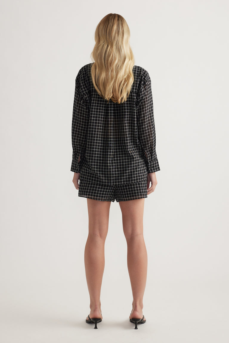 Back view of a model wearing an oversized black check shirt with long sleeves and black shorts