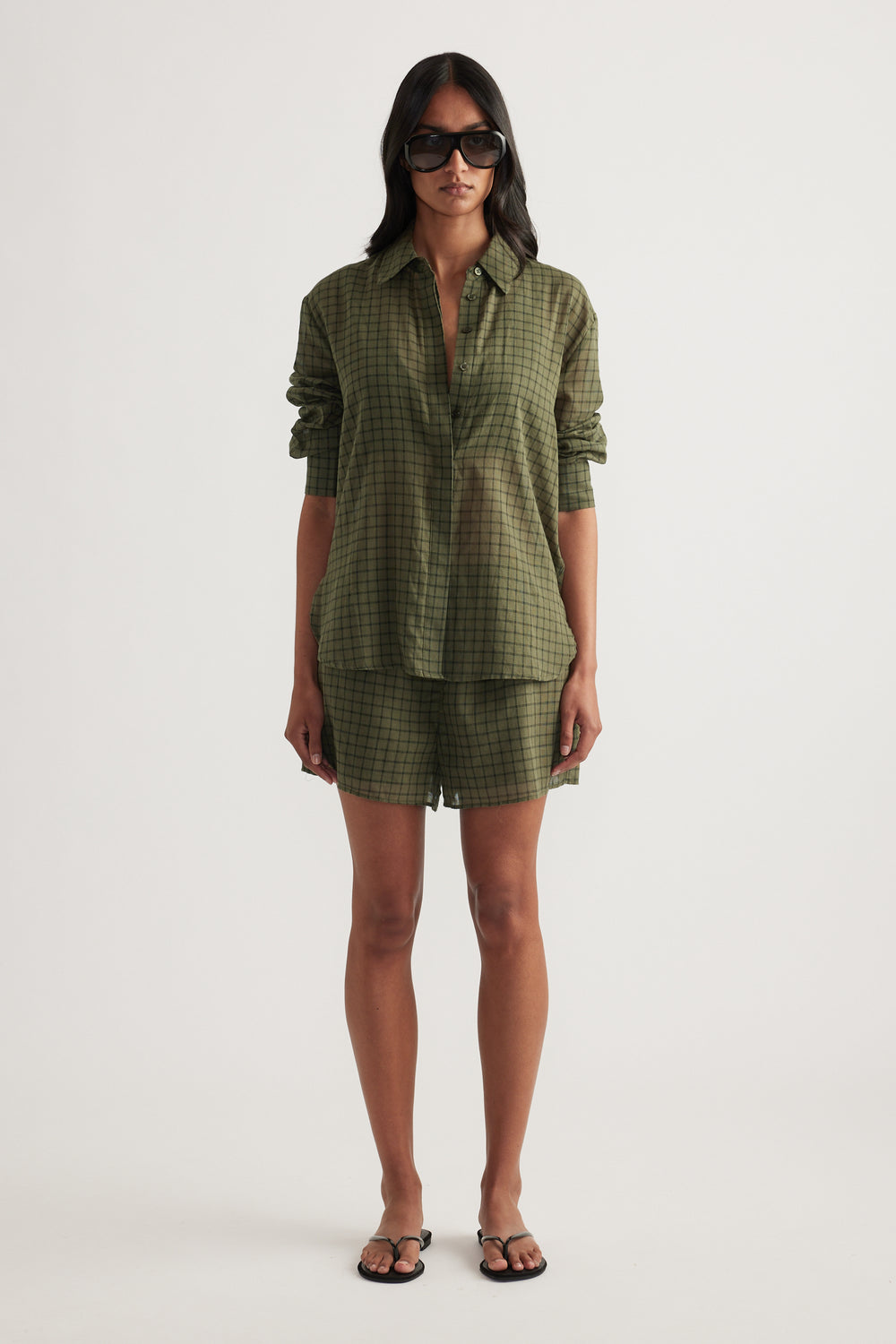 Woman wearing an oversized olive green checked shirt with matching shorts and flat sandals