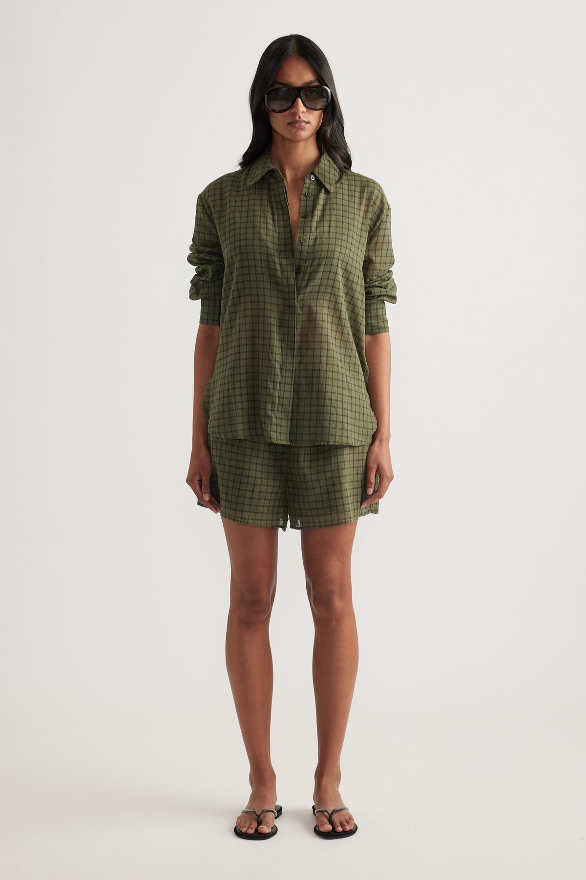 Woman wearing an oversized olive green checked shirt with matching shorts and flat sandals