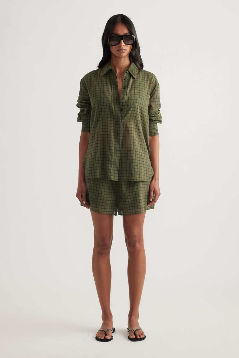 Woman wearing an oversized olive green checked shirt with matching shorts and flat sandals