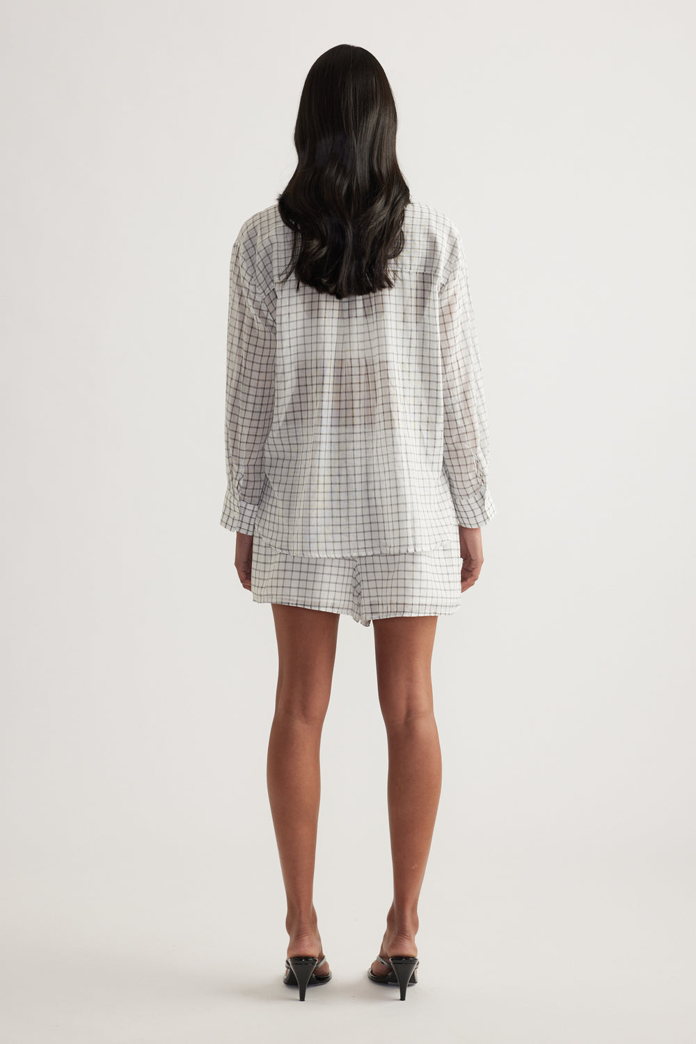 Back view of a model wearing an oversized checked shirt with long sleeves and a collared neckline