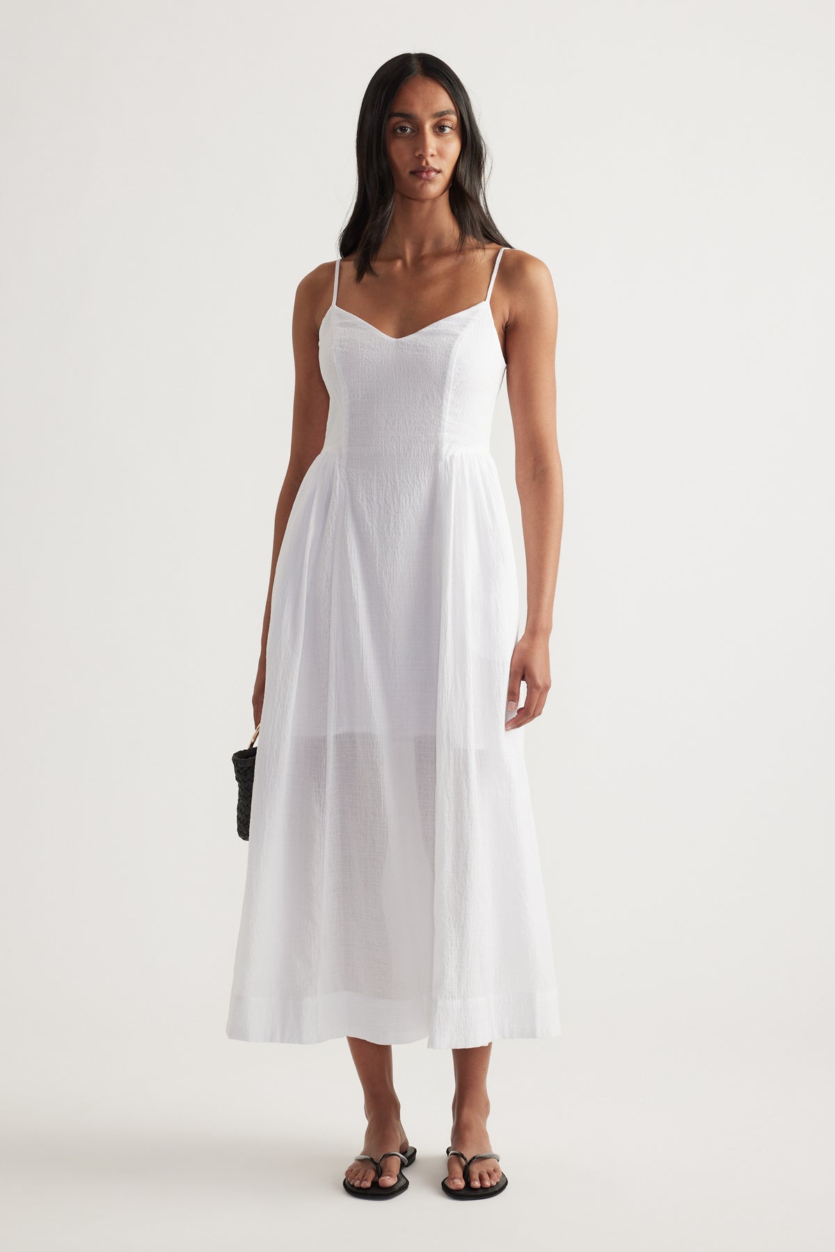 Woman wearing a white V-neck midi dress with thin straps, cinched waist and flowing fit and flare skirt