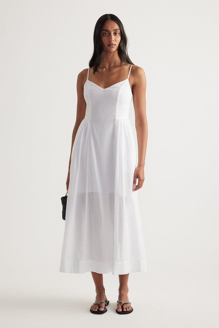 Woman wearing a white V-neck midi dress with thin straps, cinched waist and flowing fit and flare skirt
