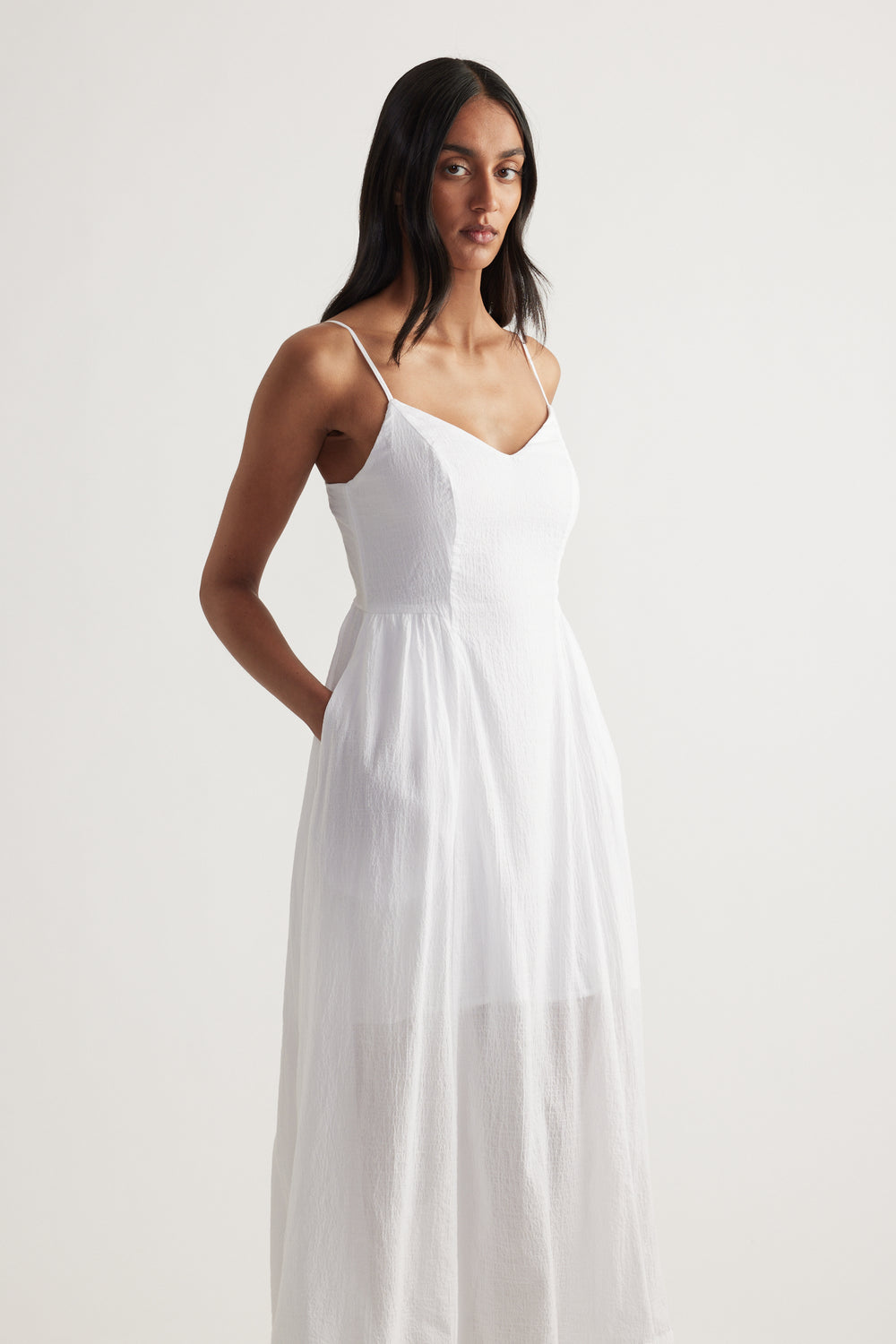 Woman wearing a white V-neck midi dress with thin straps, cinched waist and flowing fit and flare skirt