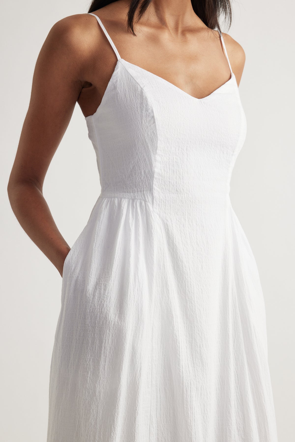 Woman wearing a white V neck midi dress with thin straps, cinched waist and flowing fit and flare silhouette