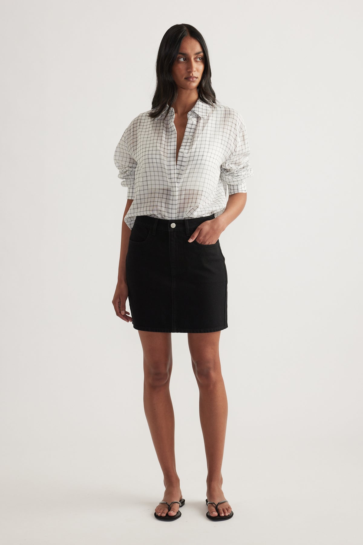 Woman wearing a high rise black denim mini skirt with a white check shirt and sandals