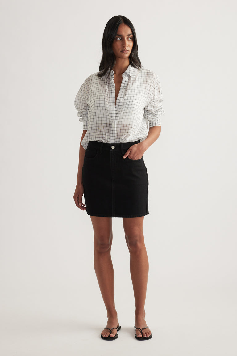 Woman wearing a high rise black denim mini skirt with a white check shirt and sandals