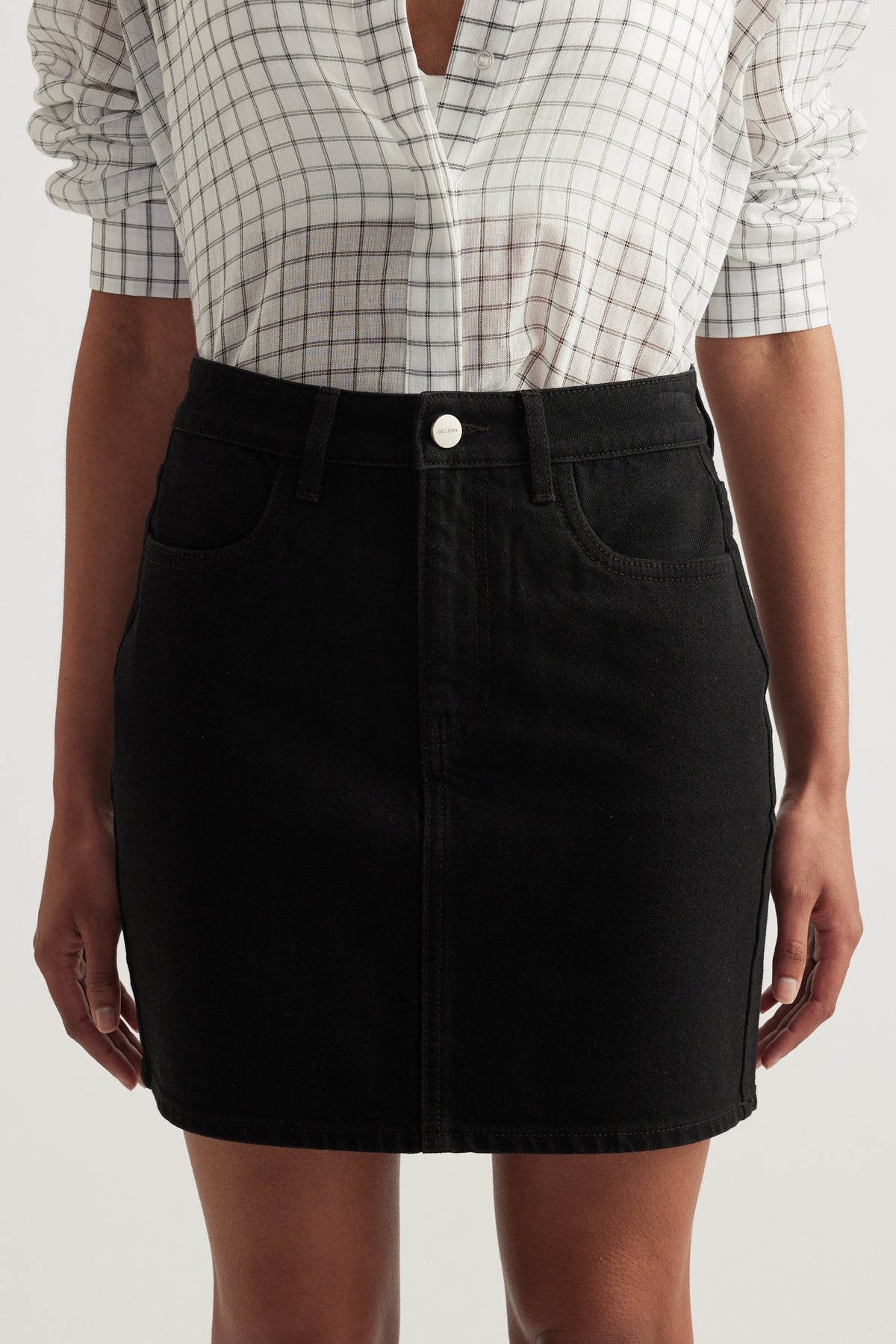 Woman wearing a black high rise denim mini skirt with a white checked blouse