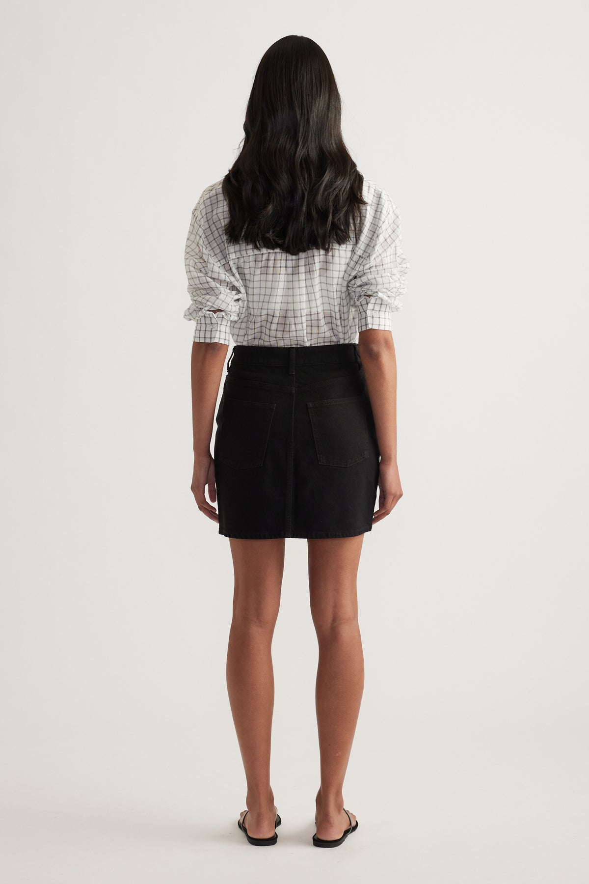 Back view of a woman wearing a black high rise denim mini skirt with an above the knee A line silhouette