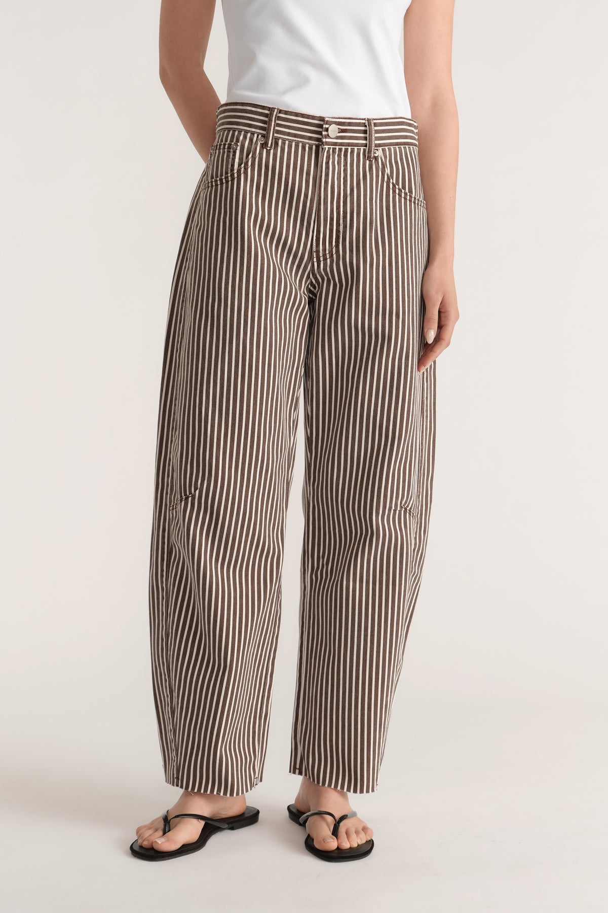 Woman wearing brown and white striped barrel leg jeans with a cinched adjustable waistband and raw hems