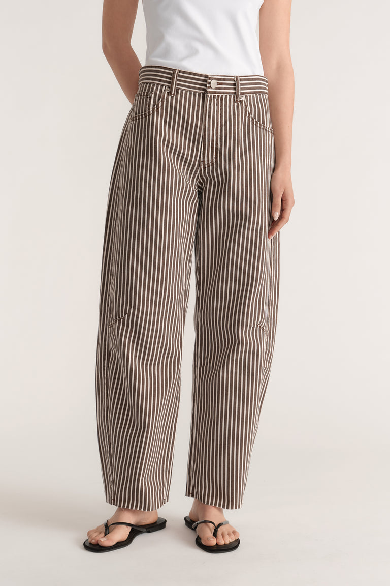 Woman wearing brown and white striped barrel leg jeans with a cinched adjustable waistband and raw hems