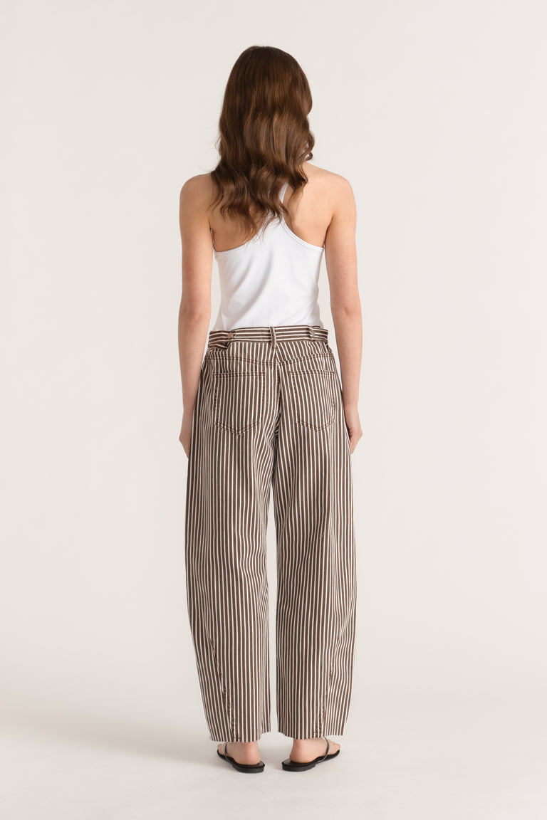 Woman seen from behind wearing brown and cream striped cinched barrel-leg jeans with an ankle-length raw hem