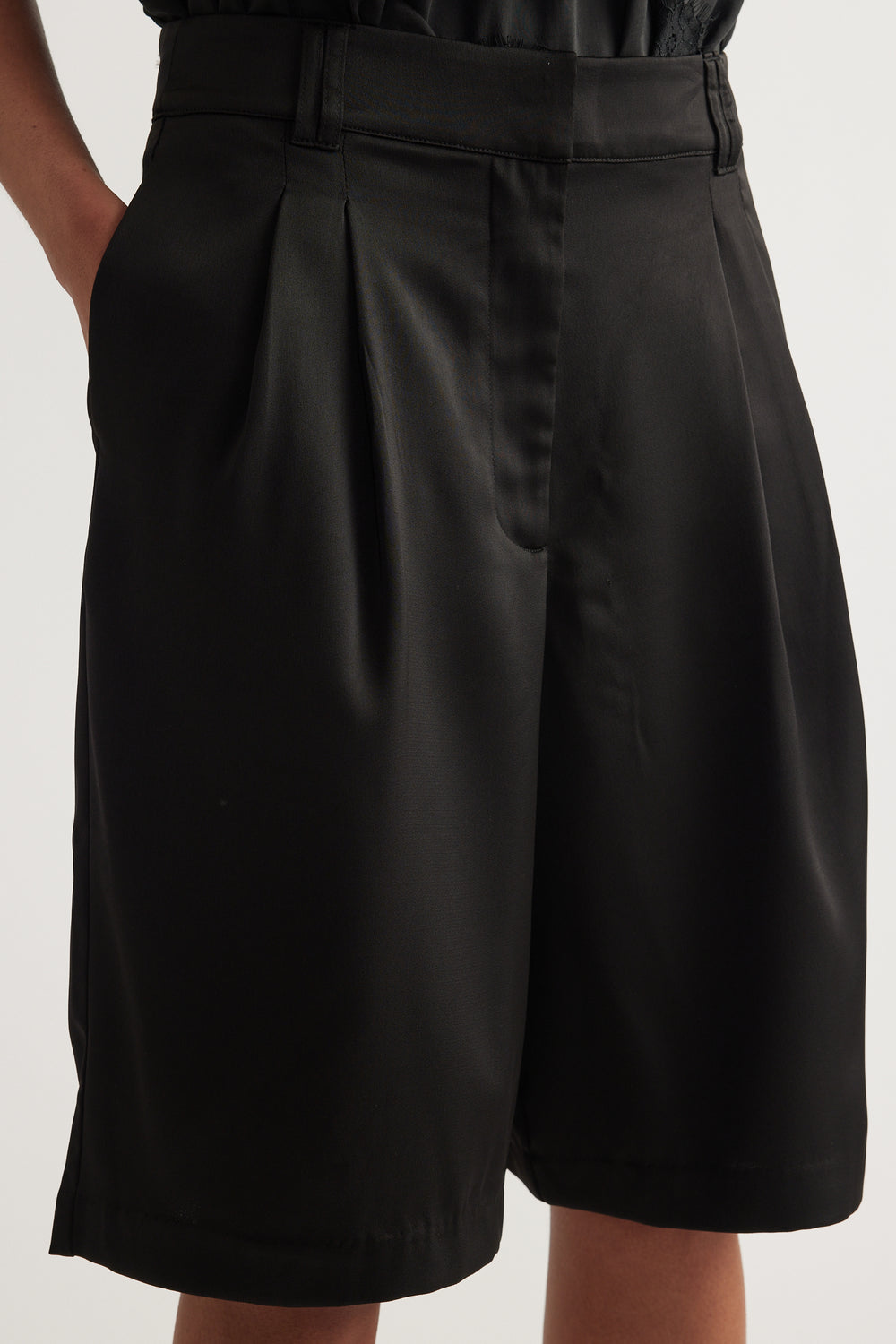 Woman wearing black satin tailored shorts with pleats, a mid-rise waist and above-knee hem