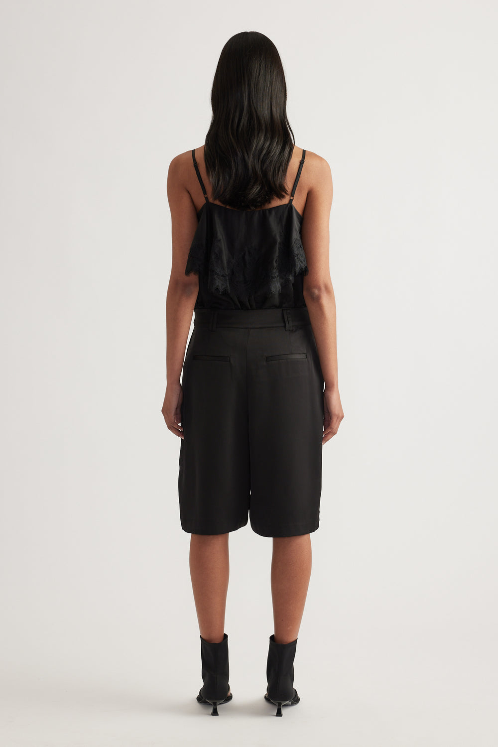 Woman viewed from behind wearing black tailored satin shorts with pleats and a black camisole