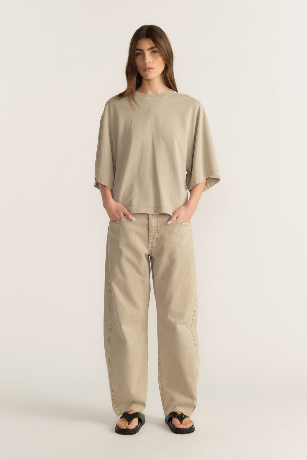 Woman wearing a beige oversized tee with relaxed barrel-leg jeans and black sandals